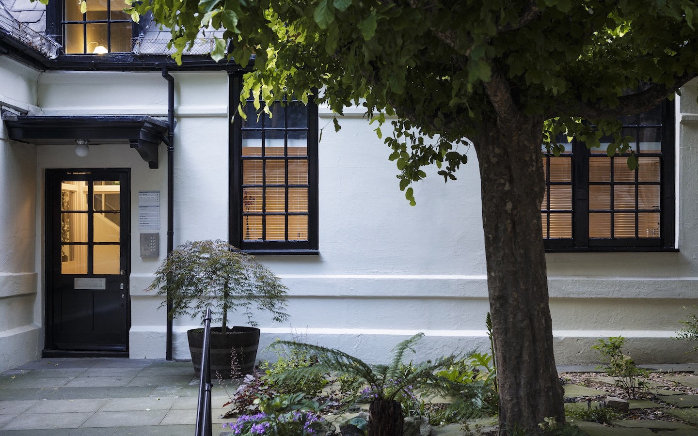 The front door for Kate Le Versha therapy in Farringdon a white building with black front door and widow frames with trees outside